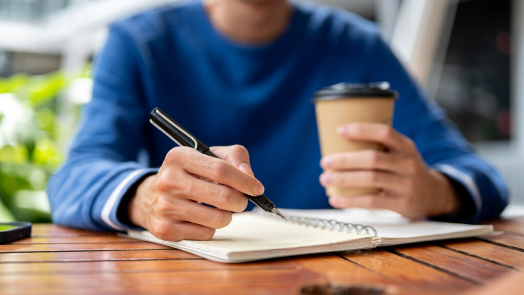 Leader writing in a notebook with coffee, representing structured routines and sustainable leadership systems